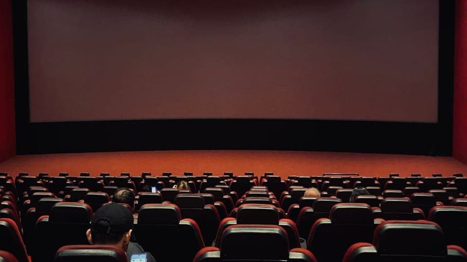 Salle de cinéma avec des rangées de fauteuils rouges face à un grand écran
